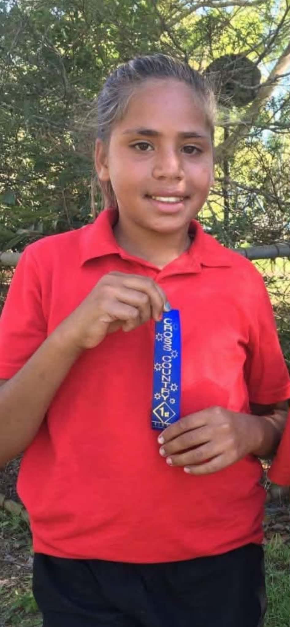 A young girl smiling holding a first place ribbon.