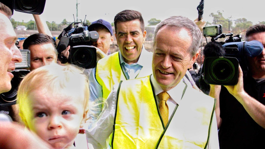 Bill Shorten in a hi-vis vest surrounded by people including cameras