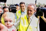 Bill Shorten in a hi-vis vest surrounded by people including cameras