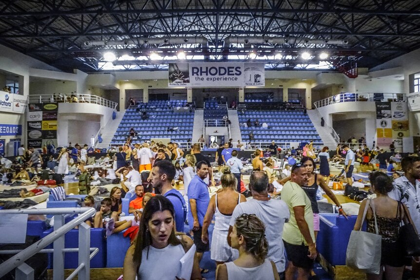 A group of evacuees sit and stand in a stadium used as a shelter on the island of Rhodes