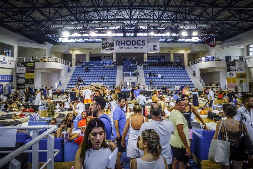 A group of evacuees sit and stand in a stadium used as a shelter on the island of Rhodes