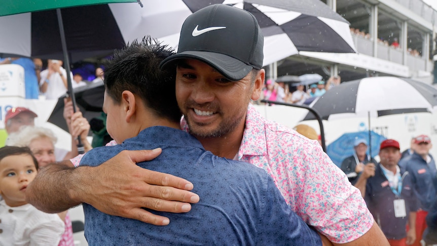 Jason Day hugs his son as he walks off a golf course in the rain.