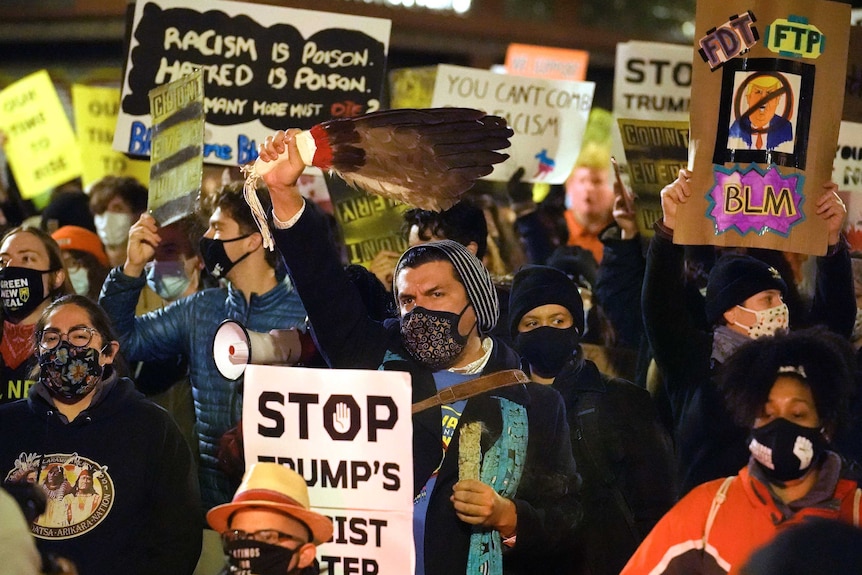 A group of masked protesters hold anti-racism signs aloft as they march through city at night.