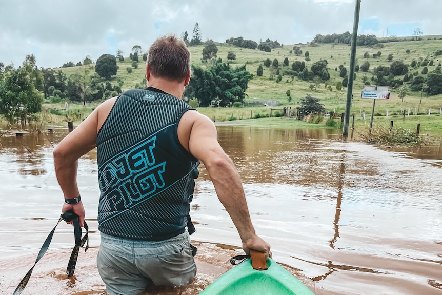 From behind image of a man wearing a life vest, pulling a dinghy through brown water body