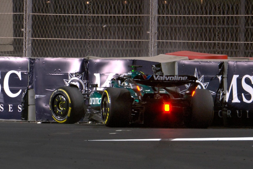 A green Aston Martin F1 car, from behind, crashed into racing barriers durnig a night race