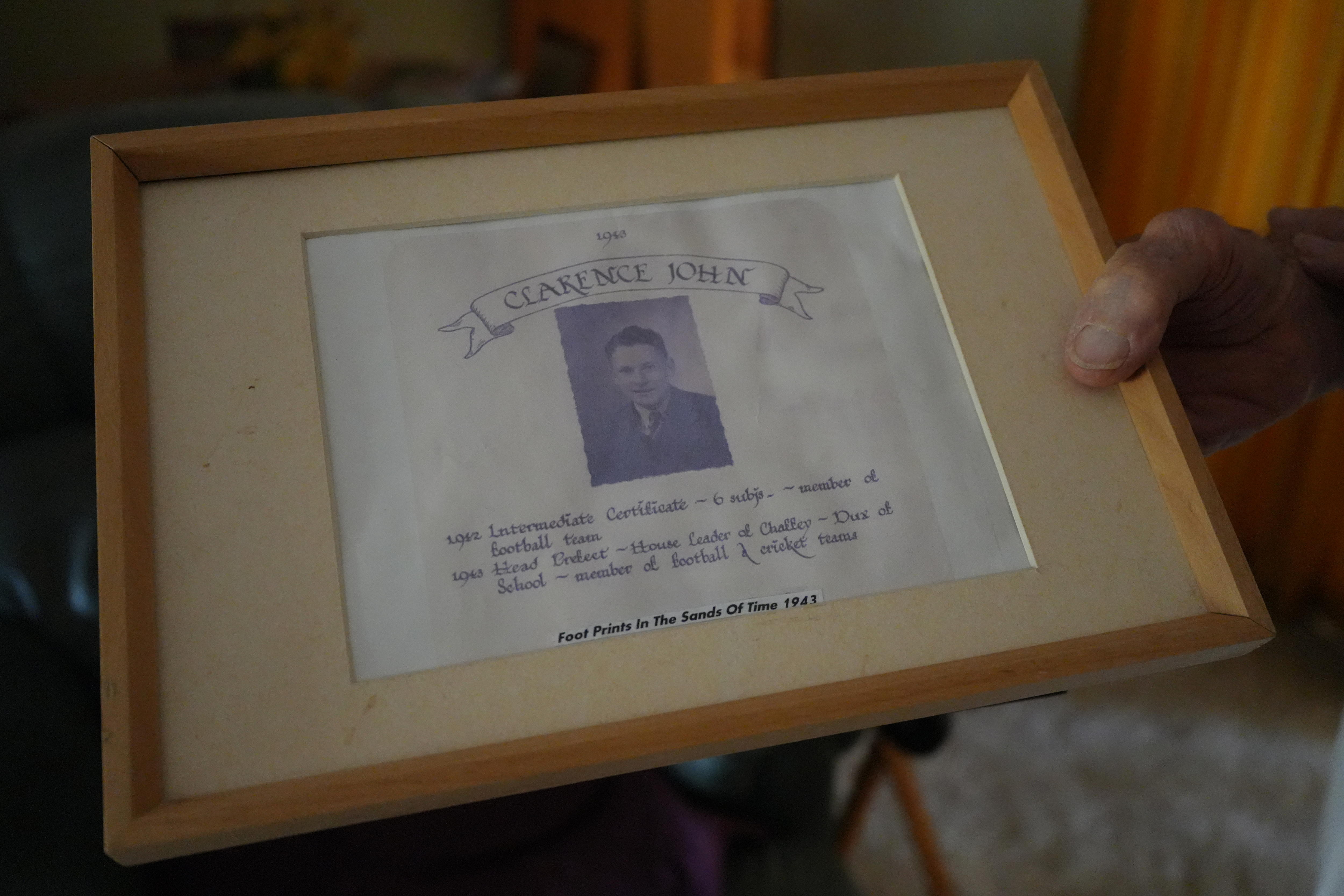 Uma mão segura um certificado de conclusão escolar emoldurado. Possui moldura de madeira e retrato em preto e branco.