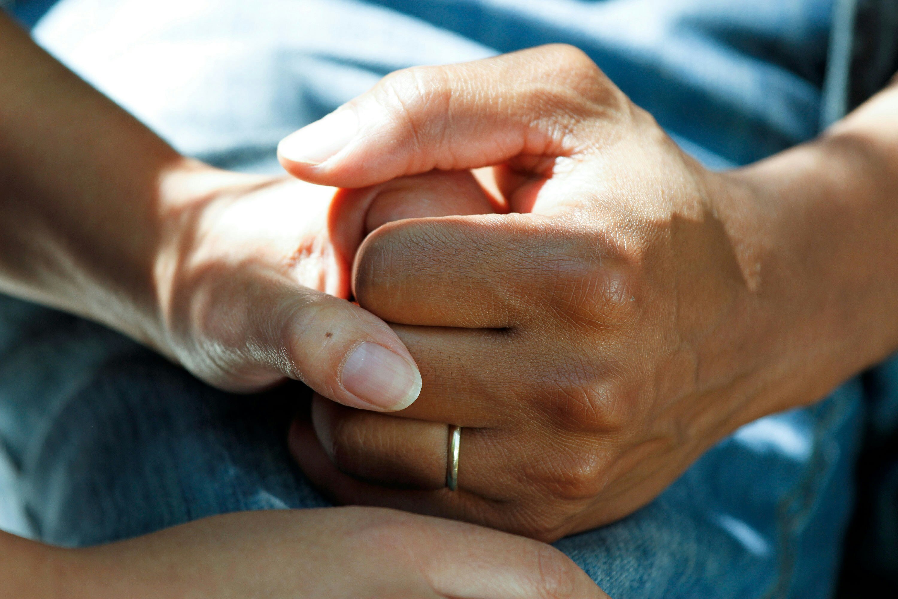 Two people's hands clasped against the background of a blue hospital gown