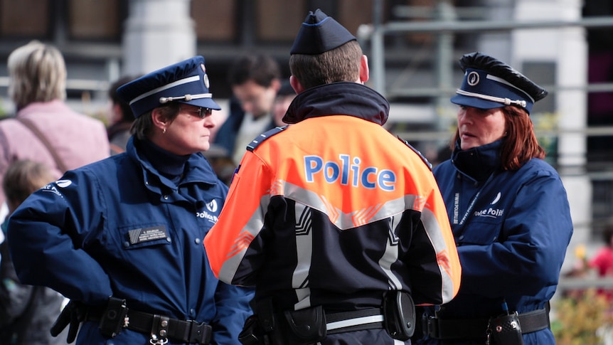 An image of three Belgian police officers—one in an orange jacket with his back to the camera.