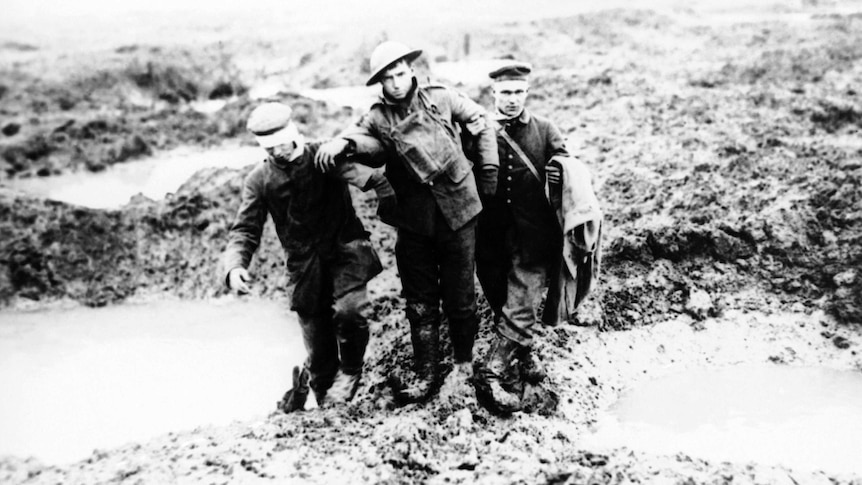 A black and white image from 1917 shows Canadian and German World War I soldiers helping one another through the mud.