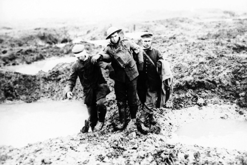 A black and white image from 1917 shows Canadian and German World War I soldiers helping one another through the mud.
