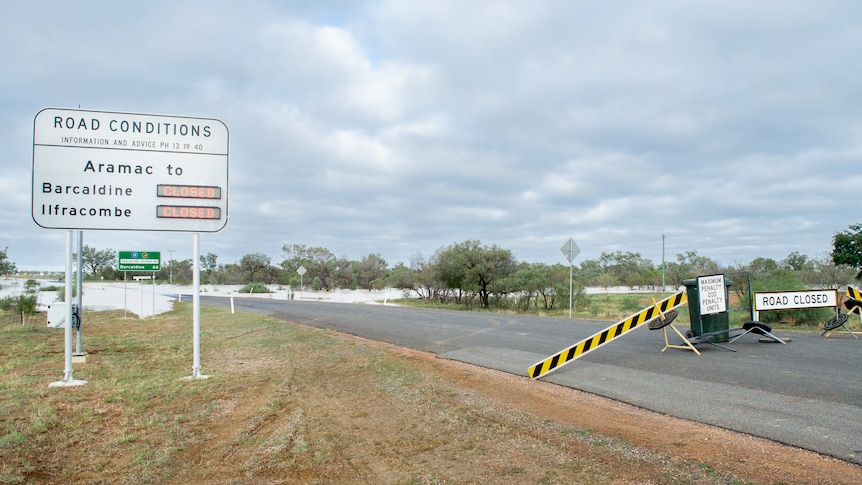 A big white sign says roads to Barcaldine and Ilfracombe are closed, and water covers the road in the background.