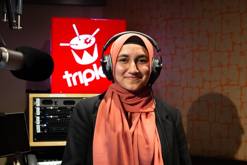 Girl wears pink headscarf and black top and looks to the camera smiling. A red box with triple j and a drum in white is lit up.