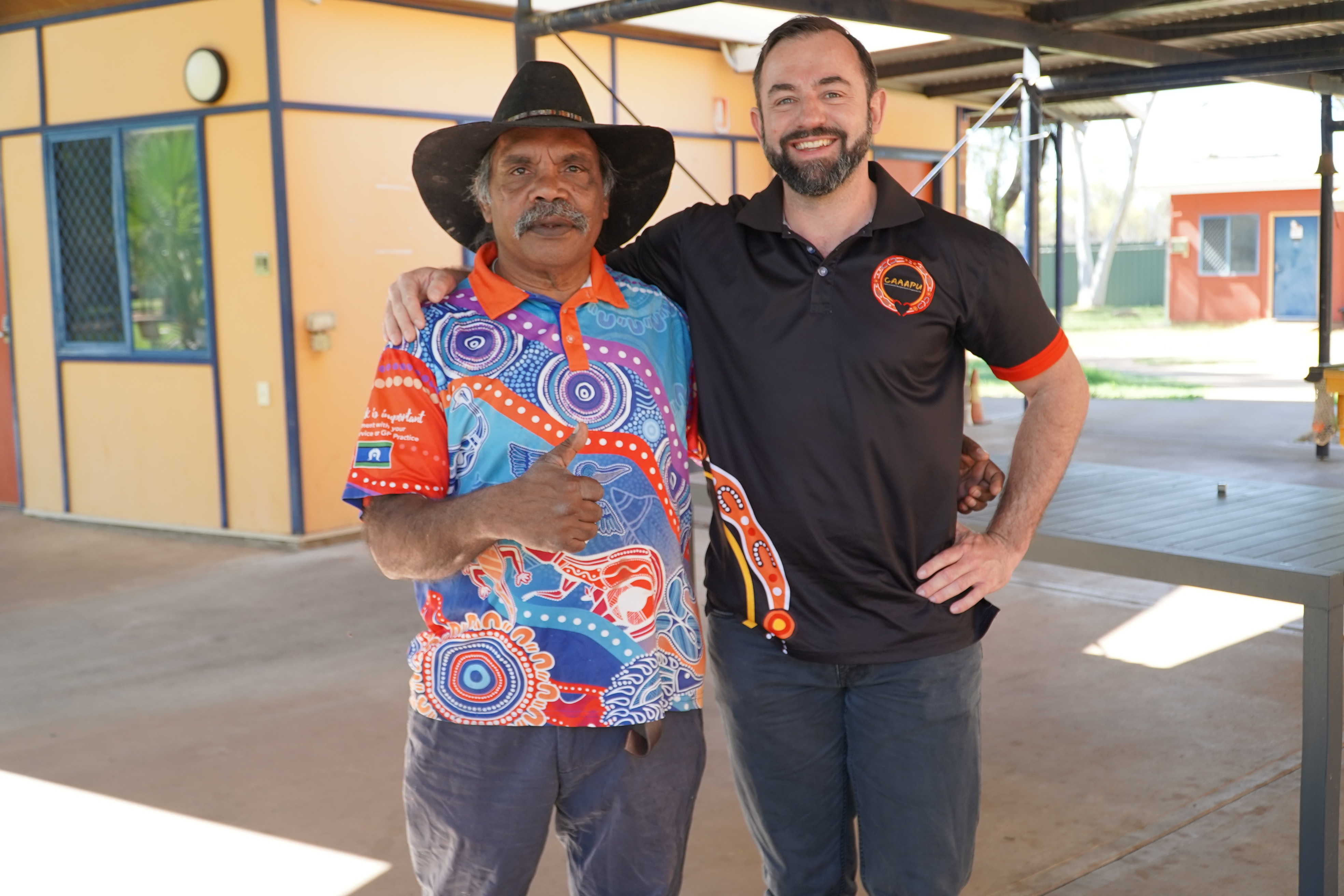 Demian wears a black shirt and has his right arm across the shoulders of Tim, who wears a black cowboy hat and colourful shirt.