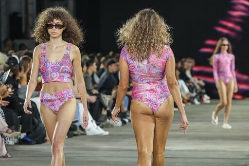 Three models in swimsuits walking down the runway in different directions