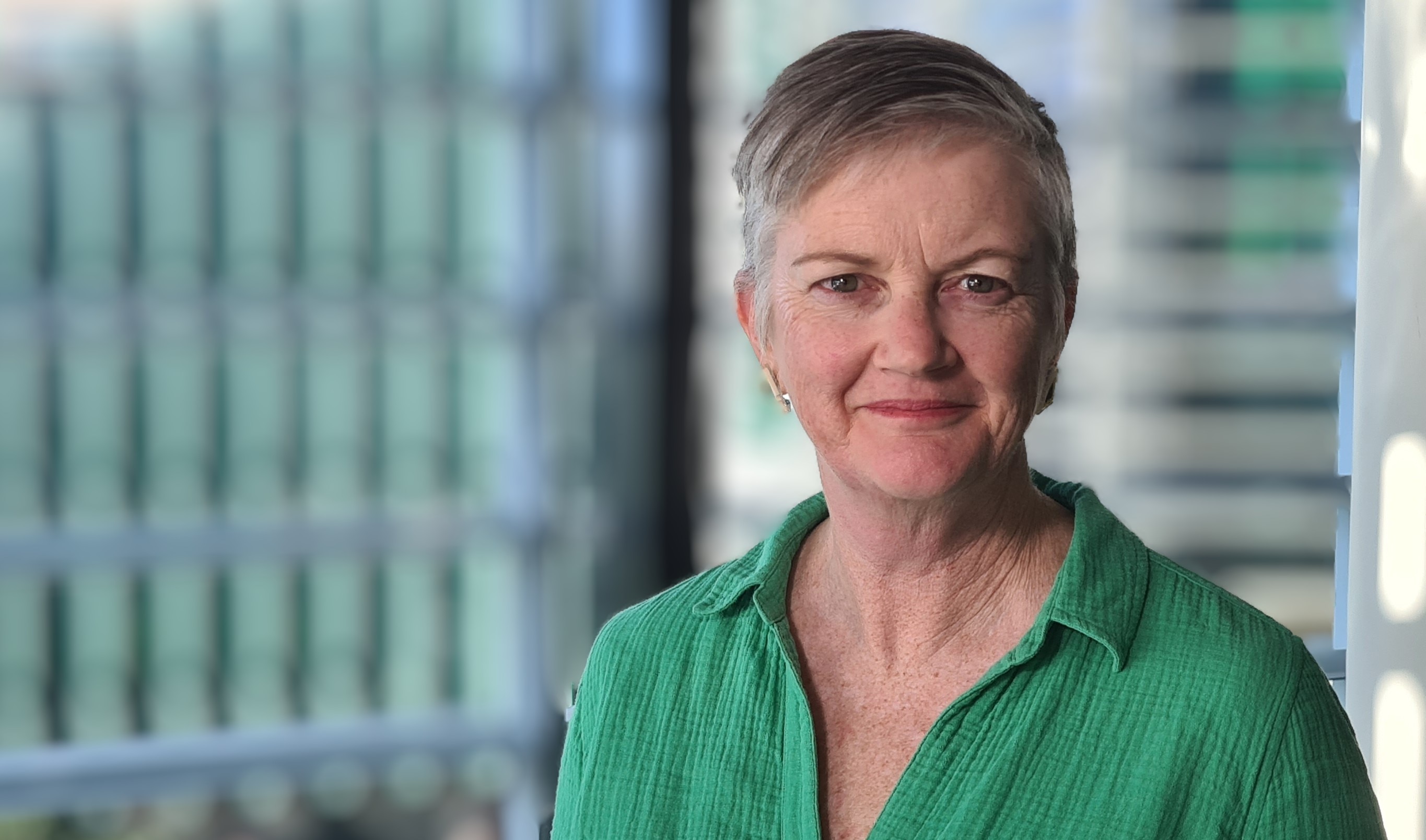 A woman with short grey hair wearing a green shirt smiling at the camera.