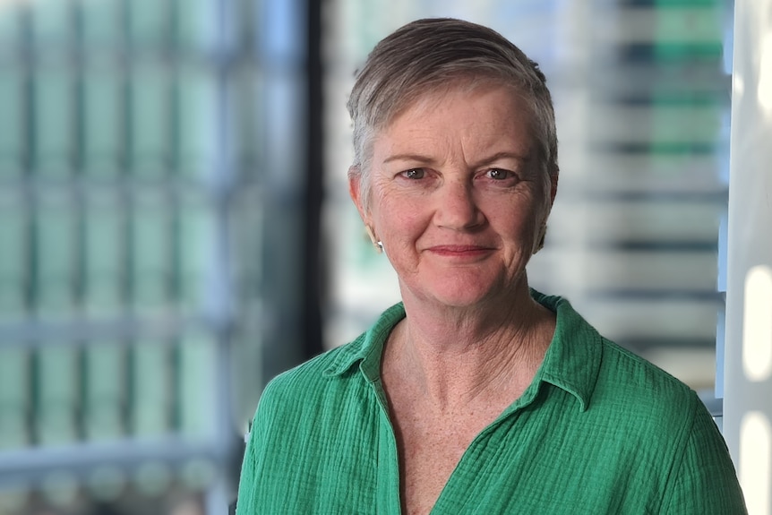 A woman with short grey hair wearing a green shirt smiling at the camera.