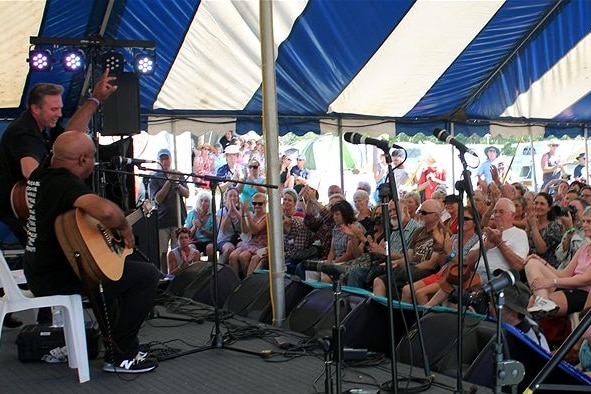 A musician at a small festival singing to a seated crowd