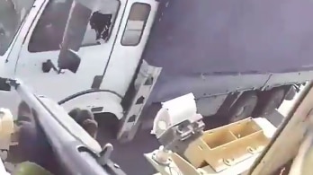 Still from video showing the barrel of a large gun in someone's hands  pointed towards a nearby truck with a hole in its window