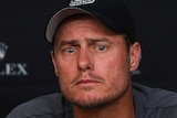 A man sits wearing a baseball cap and grey shirt