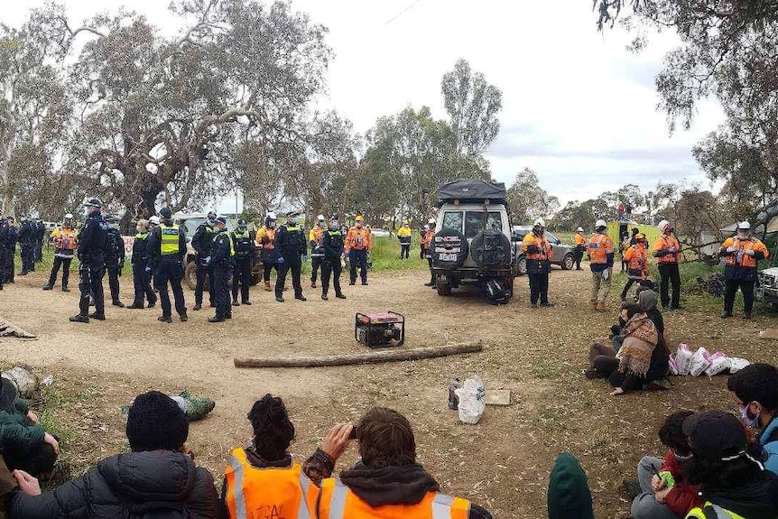 Police, workers and protesters face off at a campsite.