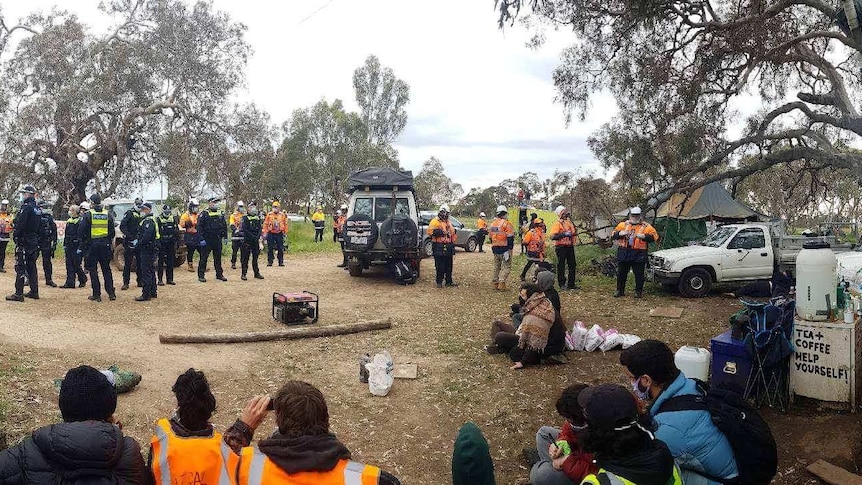 Police, workers and protesters face off at a campsite.