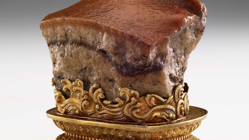 A stone sculpture of a glistening piece of pork on an ornate gold stand.