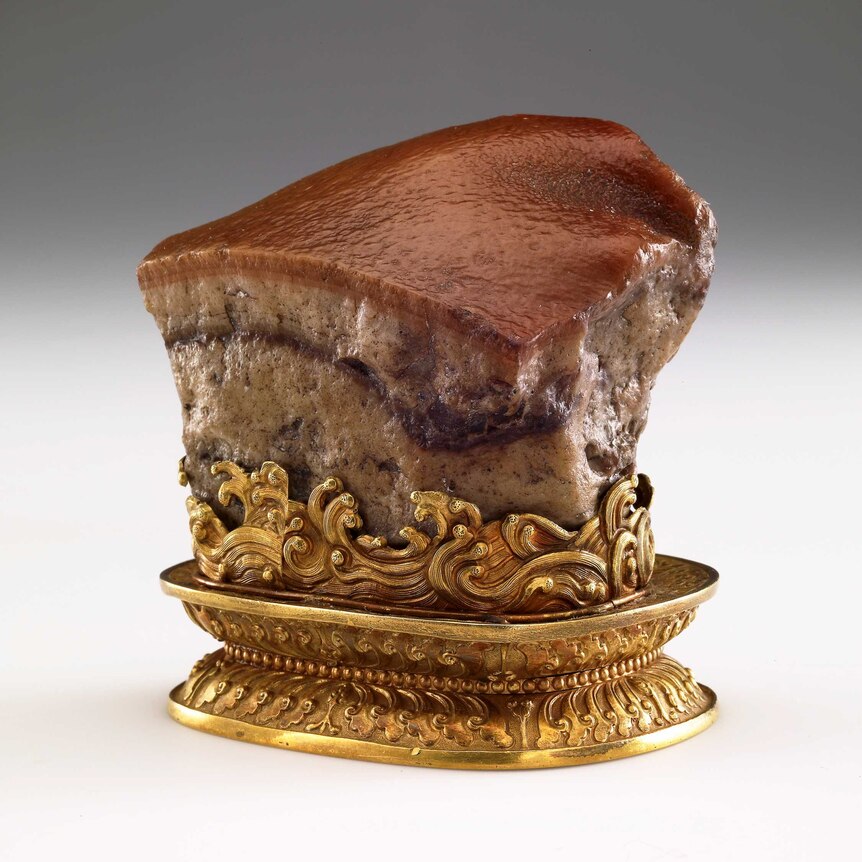 A stone sculpture of a glistening piece of pork on an ornate gold stand.