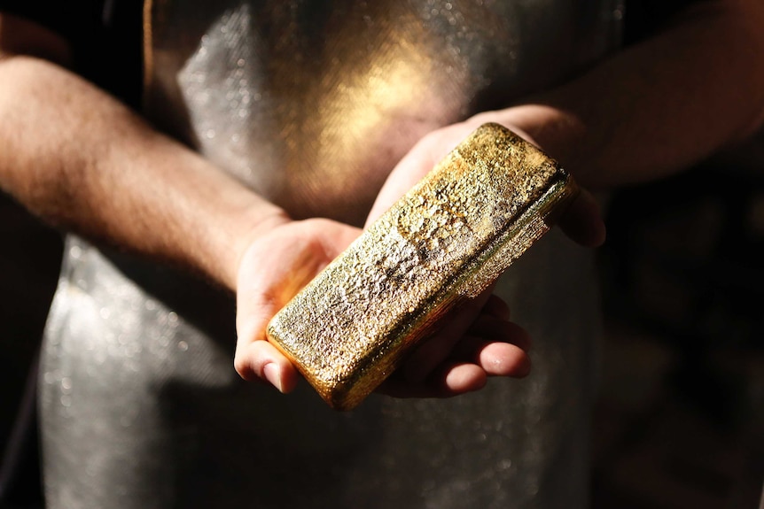 A worker holds a bar of poured gold.