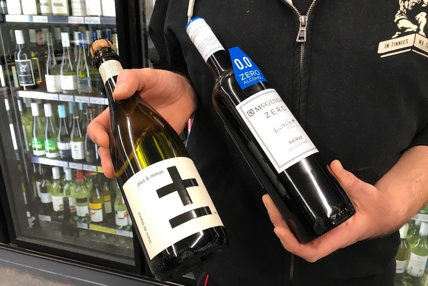 two bottles of zero-alcohol wines being held in the hand of  person in abottle shop