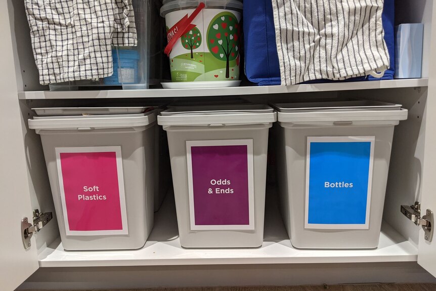 Bins labeled "soft plastics", "Odds and Ends" and "Bottles" sit in a cupboard. 