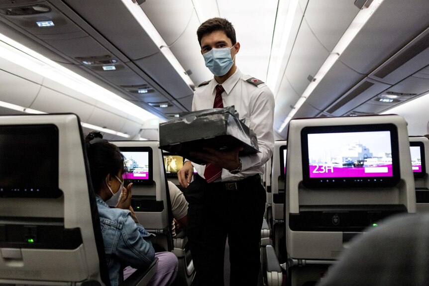 A man wearing a mask holds a tray while standing in the aisle. 