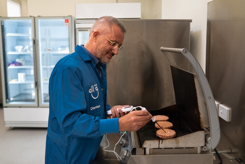 A man tests burgers on a grill with a thermometer.