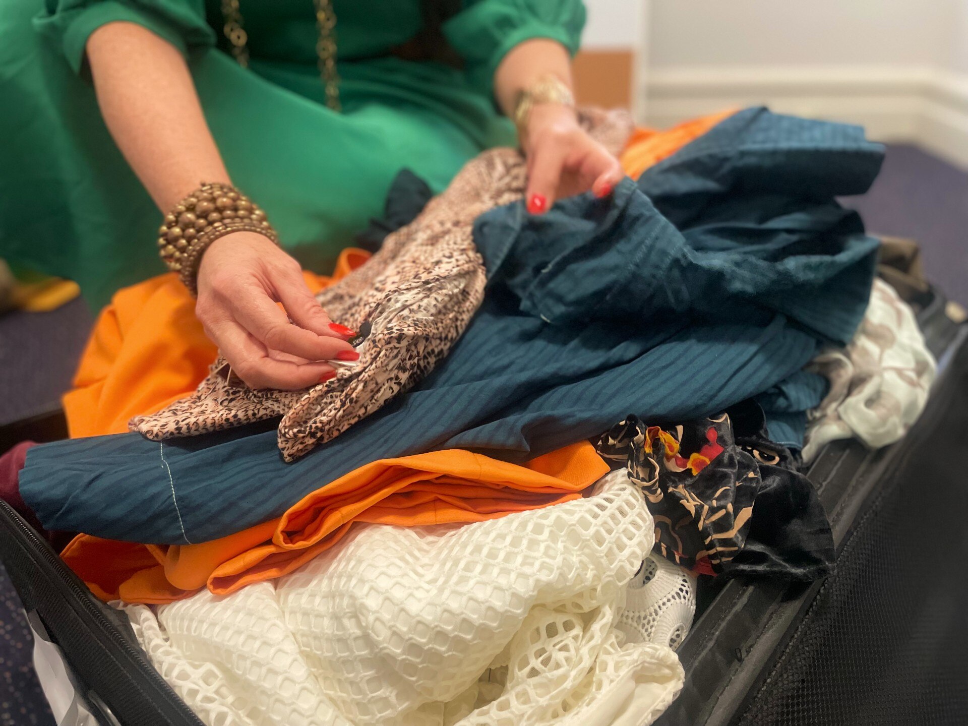 A woman in a green dress sorts through a suitcase of clothes