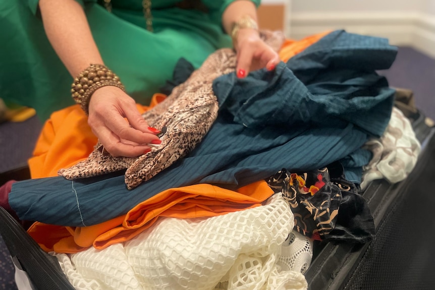 A woman in a green dress sorts through a suitcase of clothes