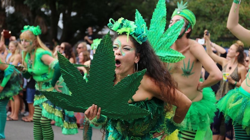 A woman dances with a group waving a large green decoration