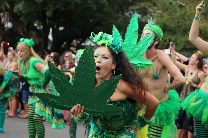A woman dances with a group waving a large green decoration