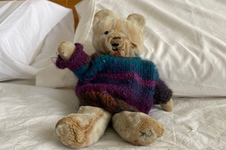 A teddy bear wearing a knitted jumper sitting on a bed.