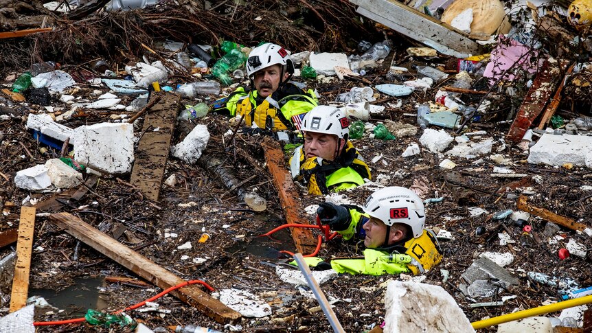 Three rescuers wade up to their necks in debris-choked floodwater in Kentucky 