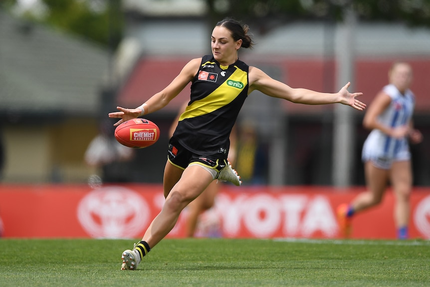 A Richmond AFLW player looks down as she prepares to kick the ball downfield during a game.