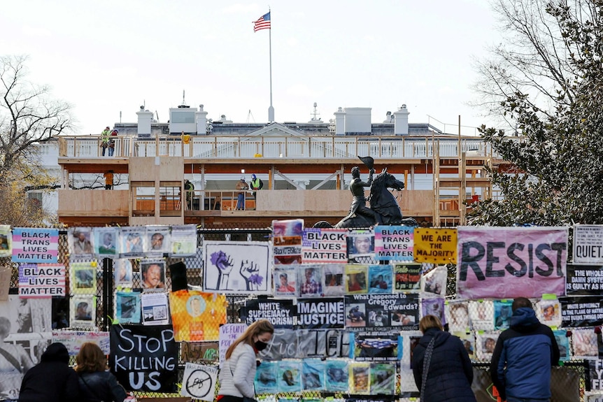 Workers construct wooden viewing stands in front of a white building, near a fence covered in Black Lives Matters posters.