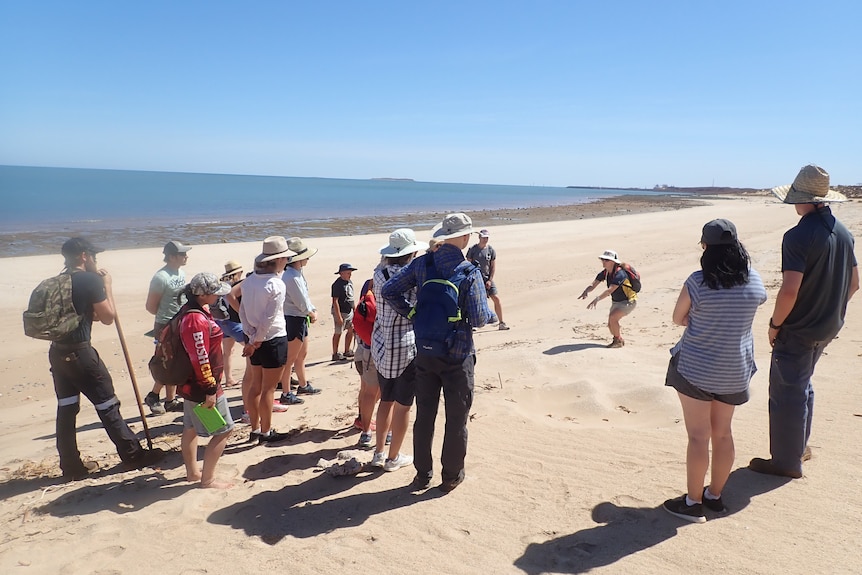 A group of people stand on a beach, next to the ocean.