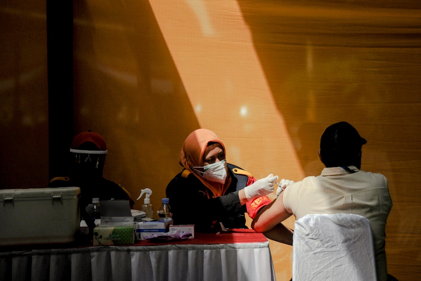 A woman wearing a hijab and mask holds onto a man`s arm who is looking away.