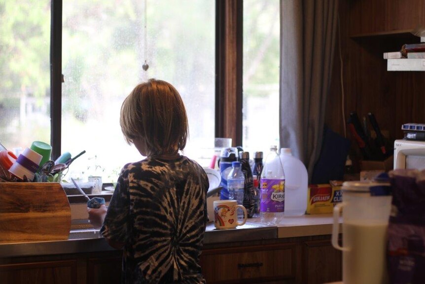A child stands at a sink in a kitchen.