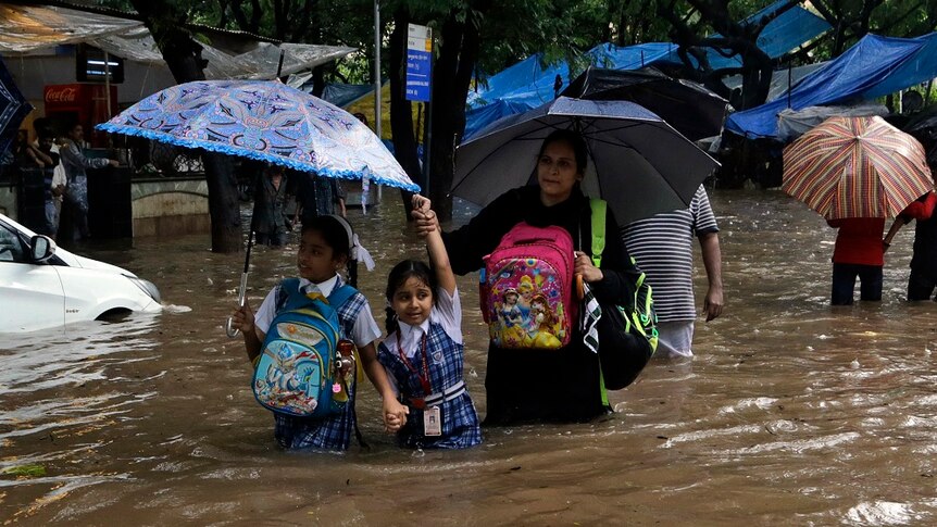 A mother leads her children through floodwaters.