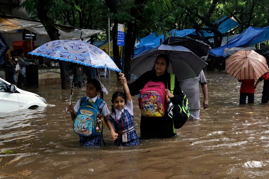 A mother leads her children through floodwaters.