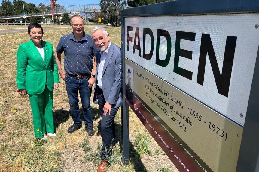 Three people stand next to a suburb sign in Canberra that says 'Fadden'.