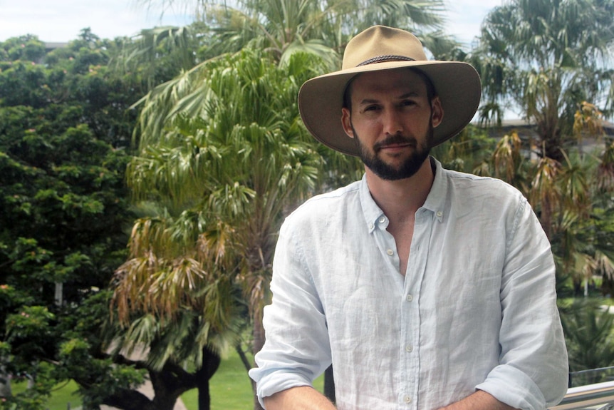 Alex Payne wears a hat and stands on a balcony