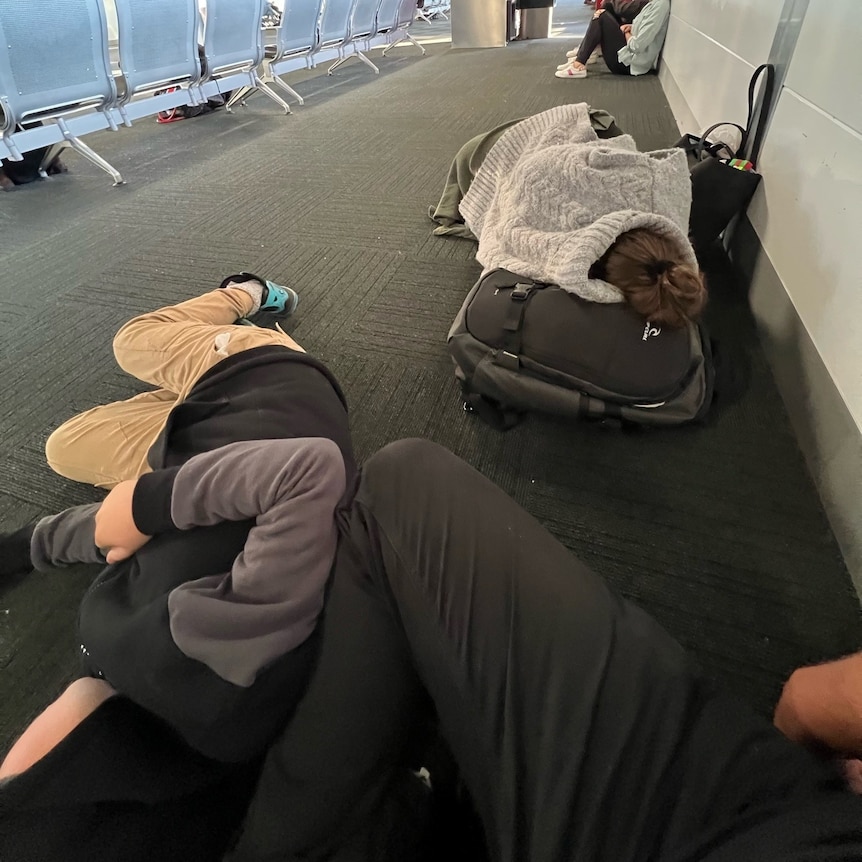 People sleeping on seats and the floor in an airport terminal.