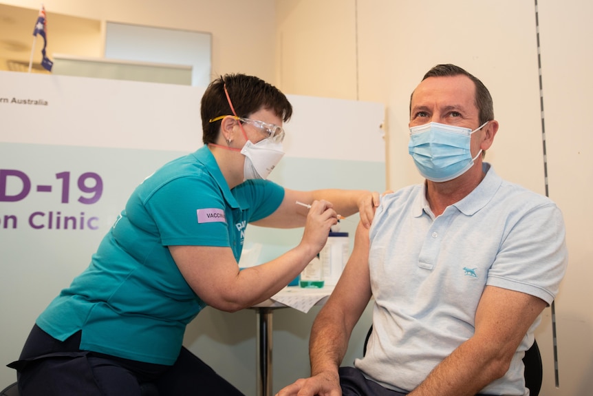 Mark McGowan is injected in his right arm at a vaccination clinic while wearing a mask