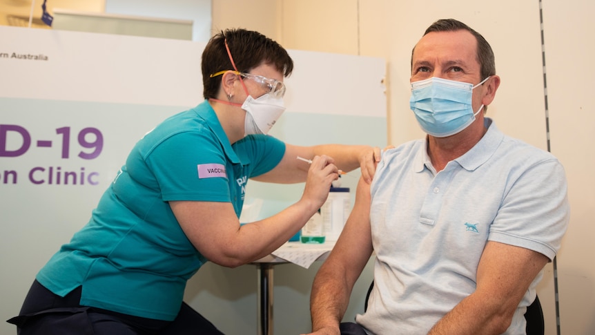 Mark McGowan is injected in his right arm at a vaccination clinic while wearing a mask